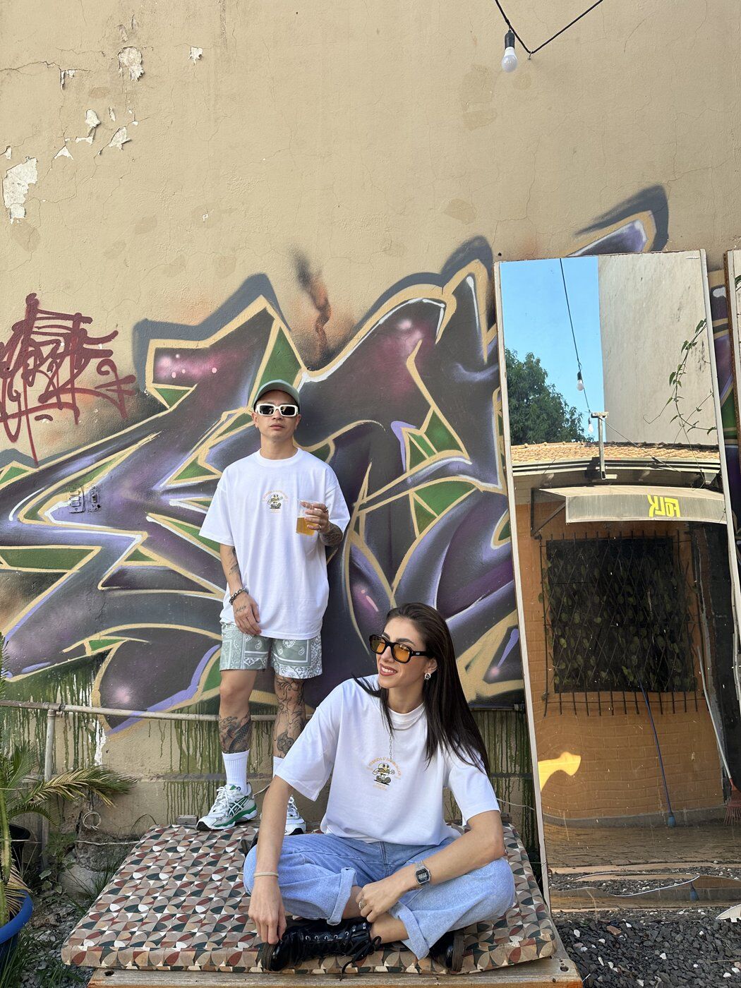 Two customers in Hybrida x Hanburger tees in front of a Paraguay graffiti wall — pop-up lifestyle shot