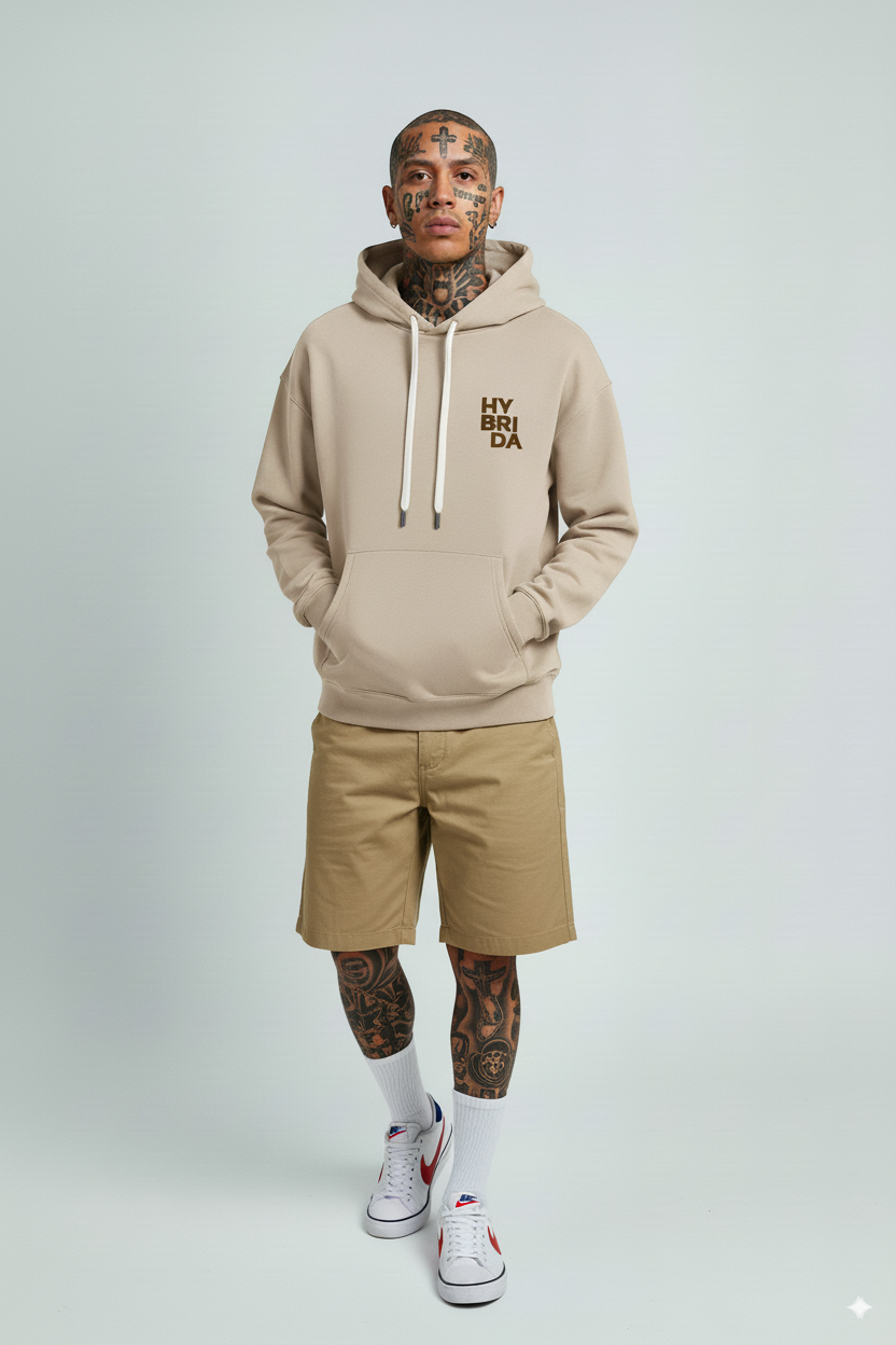 Man wearing a beige hoodie with text, beige shorts, white socks, and sneakers on a light gray background